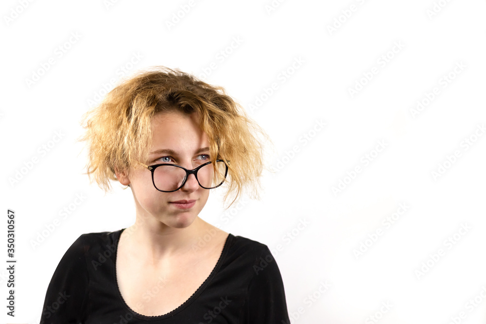 Close-up of a funny girl student in glasses with a strange hairstyle looks away, on a white background. Concept of emotions and youth