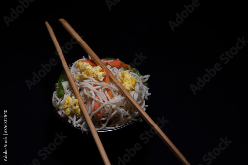 A bowl of steamed noodles and vegetables in a black copy space background. Food photography.
