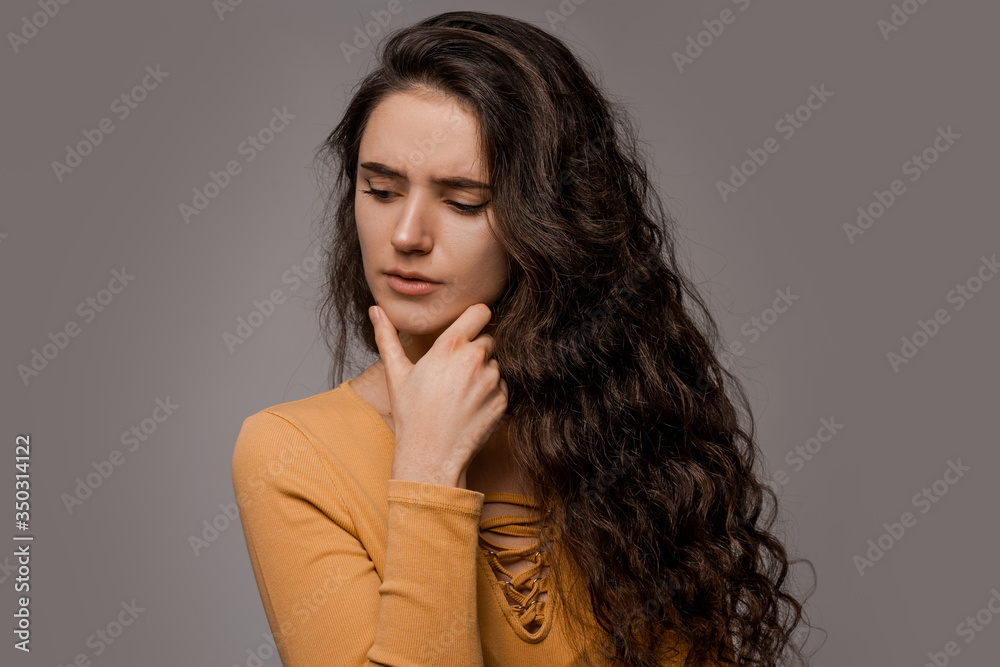 Thinking creative person with long curly hair over grey background, wearing yellow. Close portrait of pensive woman clenched her eyebrows and tensed in thought. Philosopher concept Thinking creative person with long curly hair over grey background, wearing yellow. Close portrait of pensive woman clenched her eyebrows and tensed in thought. Philosopher concept