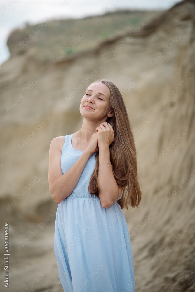 Beautiful young blonde with long hair walks along the sandy beach in a long light dress