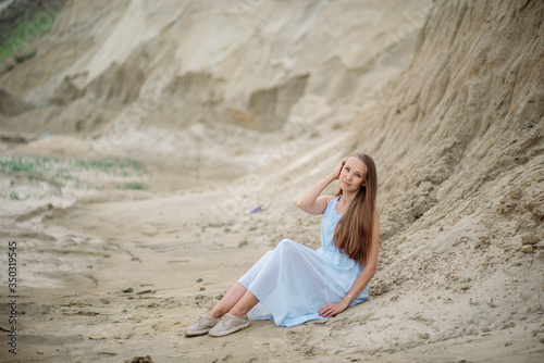 Beautiful young blonde with long hair walks along the sandy beach in a long light dress
