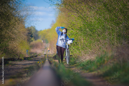 Bike trip on tracks, relax during a pandemic, girl in a white hoodie with a mask, nature of trees, bushes © Krzysztof