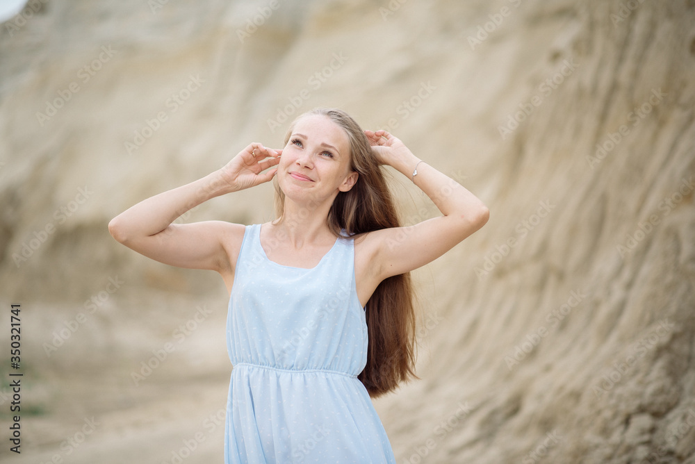 Beautiful young blonde with long hair walks along the sandy beach in a long light dress Beautiful young blonde with long hair walks along the sandy beach in a long light dress