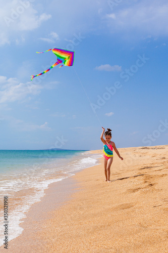 Child playing with a kite while running along the beach, in a summer sunny day. Have fun with your family during the holidays. Happy little girl launches a kite, summer vacation