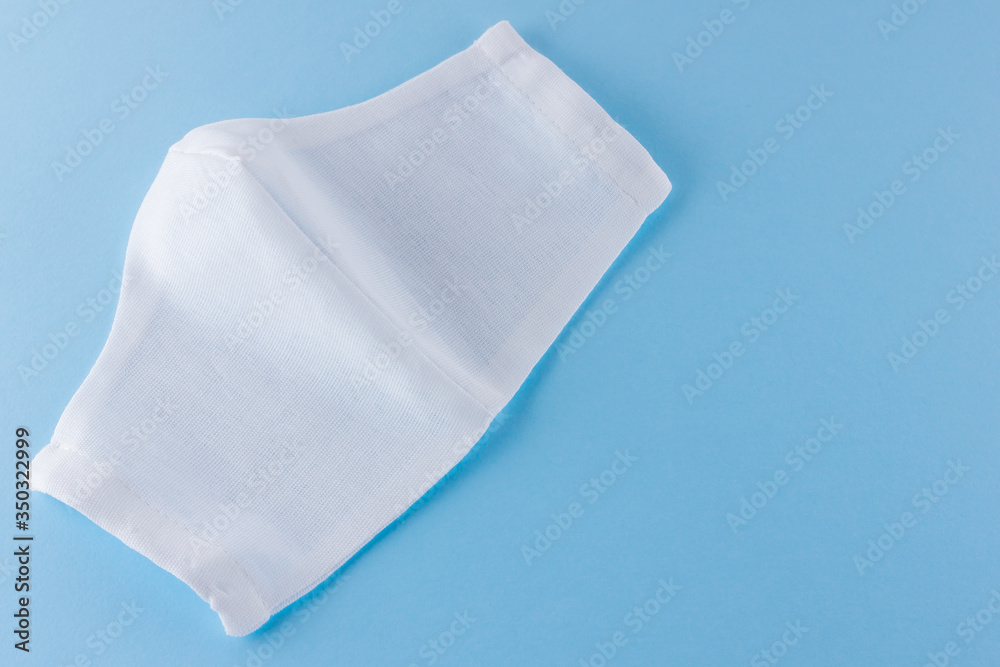 White antivirus mask. Protective gauze mask on a blue background. Handmade medical protective mask from cotton. Protective face mask made of gauze. Top view. Copy space White antivirus mask. Protective gauze mask on a blue background. Handmade medical protective mask from cotton. Protective face mask made of gauze. Top view. Copy space