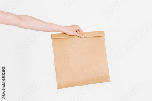 The courier holds a paper bag with food on an isolated white background. Fast and free delivery. Online stores