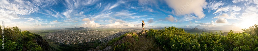 The climber is standing on top of a high mountain in the background of a stunning landscape and sunset. Mauritius Island, panorama