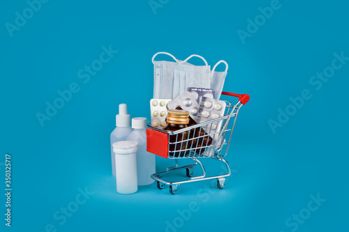 Medicine bottles with pills and medical masks in a shopping cart on a blue background.