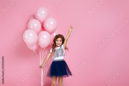 Smiling adorable little child girl posing with pastel pink air balloons isolated over pink background. Beautiful happy kid on a birthday party. copy space