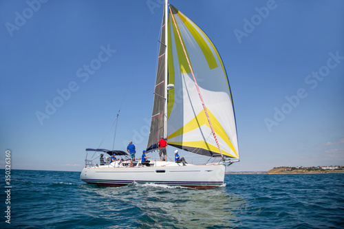 A white motor yacht with raised sails takes part in the regatta. A strong wind tipped the ship. Waves, a small wave amplify emotions at competitions. A man, a sailor, a yachtsman is lying on the bow o © Irina