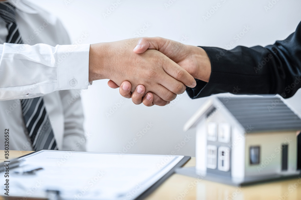 Real estate agent are shaking hands after good deal and giving house, keys to customer after discussing and signing contract to buy house with approved application form