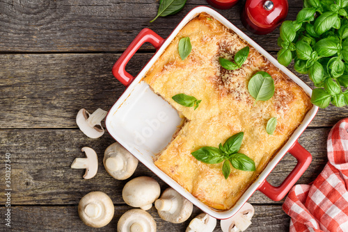 Lasagna in red ceramic form. Traditional Italian dish with meat, mushrooms, cheese and tomatoes. Copy space. Top view.