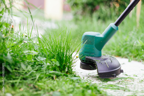 Mowing high grass with electric trimmer. Lawn care concept photo