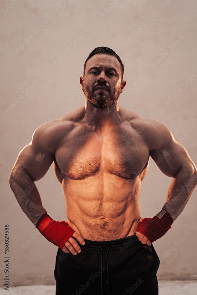 Fototapeta premium Strong and powerful fitness coach posing in a bright studio with hand wraps on, looking serious