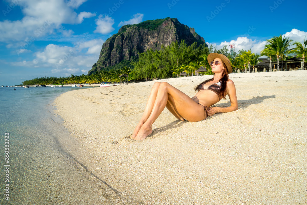 Young girl model posing against a backdrop of picturesque palms, snow-white sand, ocean, boats and mountains. Mauritius Island, Indian Ocean