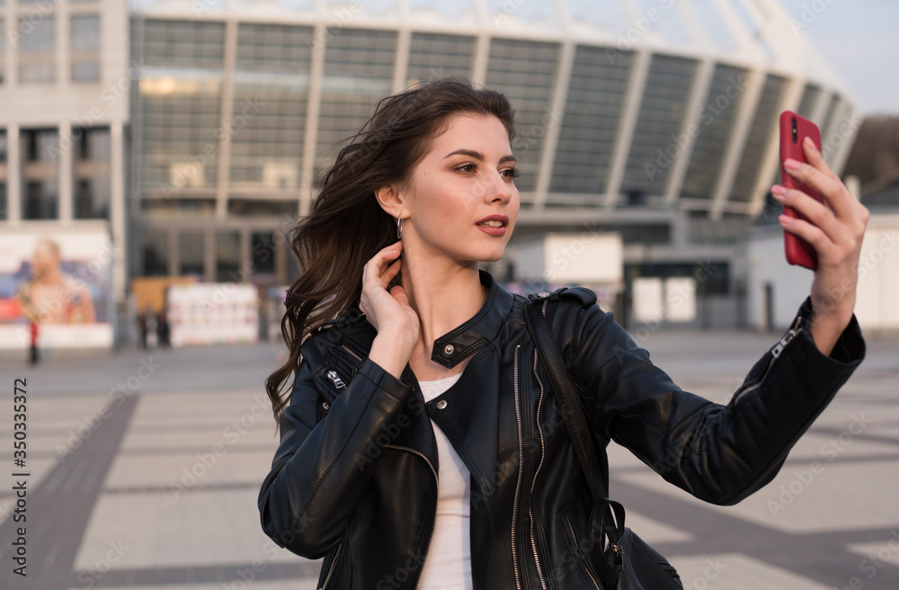 smiling young woman makes selfie in city, european woman wears leather jacket smiling young woman makes selfie in city, european woman wears leather jacket