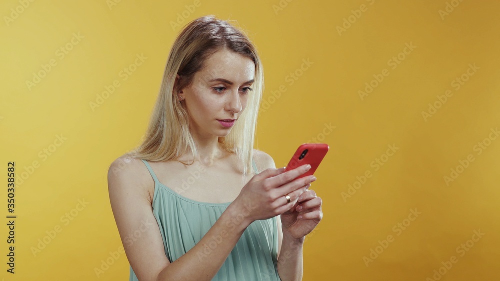 People and technology. Modern young woman using a smartphone typing message in social media laughing communicating posing at orange background. People and technology. Modern young woman using a smartphone typing message in social media laughing communicating posing at orange background.