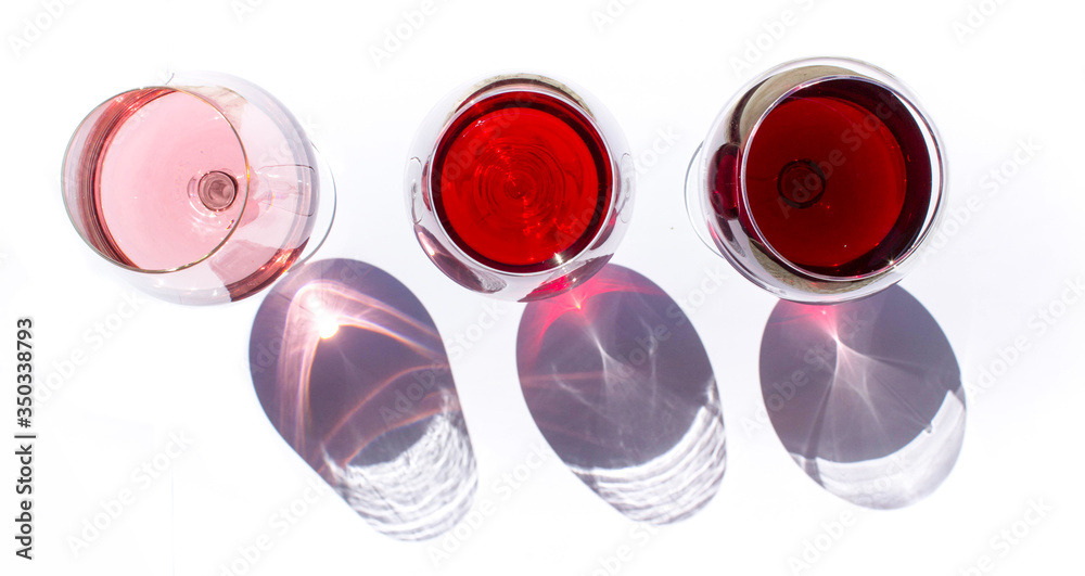 Three glasses of wine: red and pink on white background with sparkling shadows. Top view. Free copy space. Concept of organic drinks. Three glasses of wine: red and pink on white background with sparkling shadows. Top view. Free copy space. Concept of organic drinks.