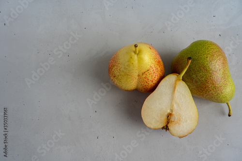 Two whole pears and one pear half are laying in a group on cement surface on the right side