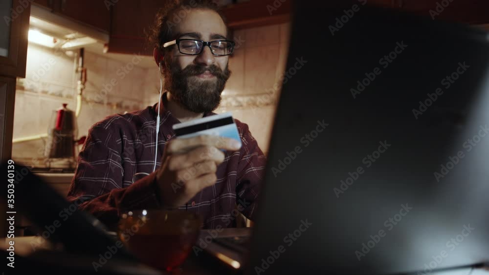 E-Commerce concept. Happy and smiling man is making a card payment through laptop to pay bills. Easy pay using digital gadget. Slow motion, 4k. E-Commerce concept. Happy and smiling man is making a card payment through laptop to pay bills. Easy pay using digital gadget. Slow motion, 4k.