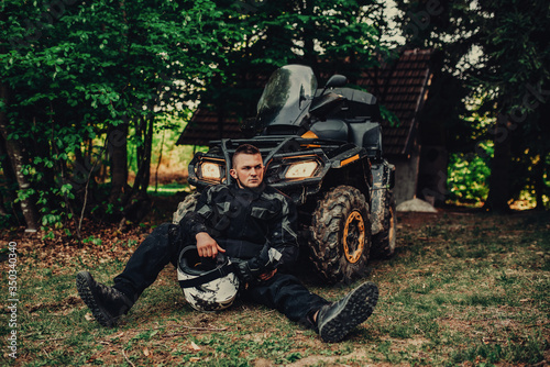 portrait of young happy man enjoying beautiful sunny day taking a break from driving a quad,atv in forest