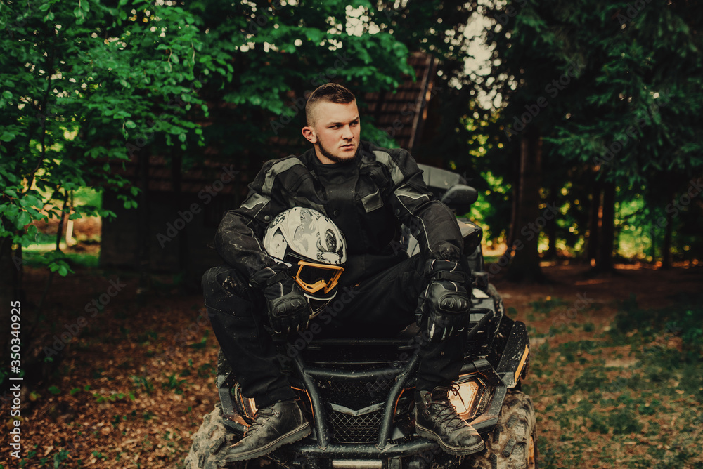Man sitting on quad in forest and preparing for ride