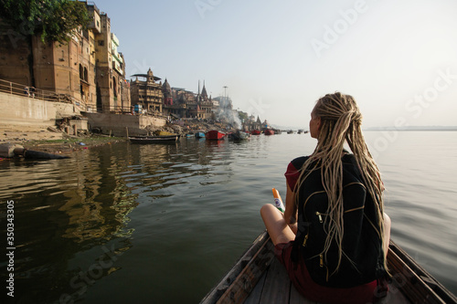 Travel woman on a boat glides on Ganges river along the shore of Varanasi, India.