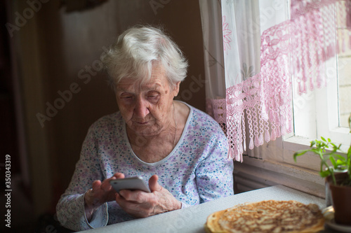 An elderly woman sits with a smartphone in her hands.