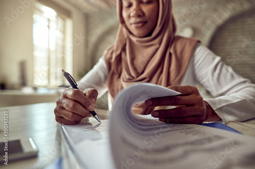 Close-up of Muslim businesswoman signing documents in the office.