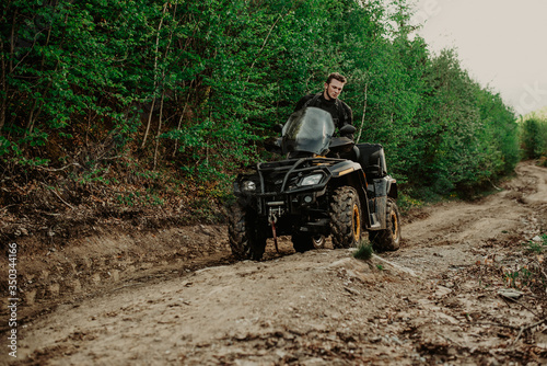A young man in a white helmet rides through the woods on a Quad bike. Extreme hobby. A trip to ATV on the road from logs. Quad Biking through the forest.