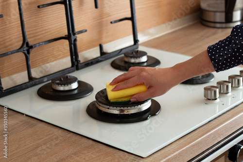 A woman washes a gas stove with a yellow sponge. cleaning the kitchen.