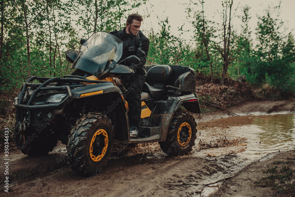 Fototapeta premium A young man in a white helmet rides through the woods on a Quad bike. Extreme hobby. A trip to ATV on the road from logs. Quad Biking through the forest.