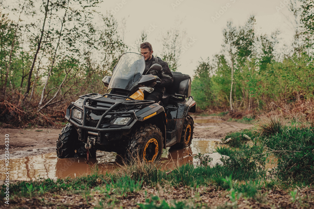 Fototapeta premium A young man in a white helmet rides through the woods on a Quad bike. Extreme hobby. A trip to ATV on the road from logs. Quad Biking through the forest.