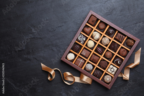 Box with delicious chocolate candies on black table, flat lay. Space for text