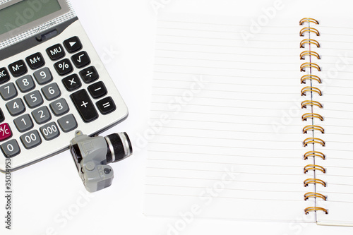 Top view of an open blank notebook, calculator and a scaled-down camera model