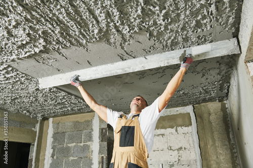 Plasterer smoothing plaster mortar on ceiling with screeder photo