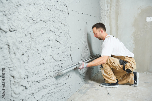 Plasterer using screeder smoothing putty plaster mortar on wall photo