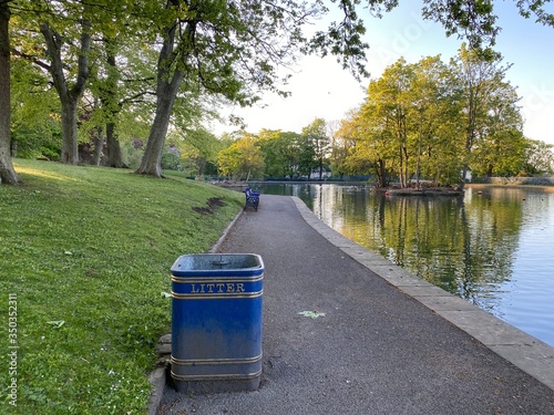 Lake edge with asphalt footpath, grassy knoll and old trees, on a late spring day in, Lister Park, Bradford, Yorkshire, England photo