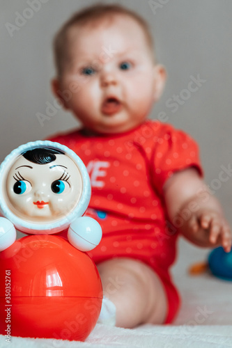 infant sitting on the white sofa and roly-poly toy lying near. photo