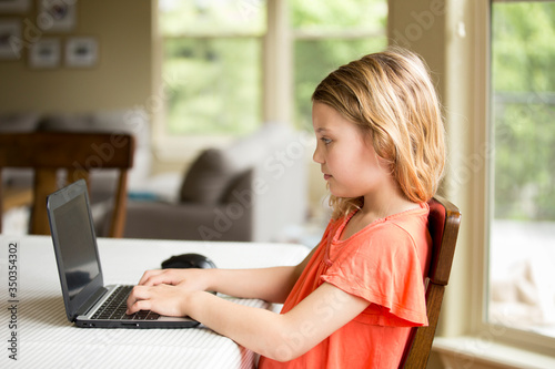 A young girl does elementary school work on a laptop computer at home