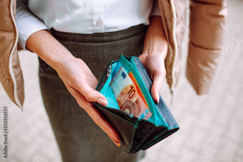 Woman wearing office suit holding almost empty open wallet with one banknote. Saving money, unemployment, low salary, financial difficulties concept.