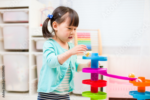 toddler girl play marble run game at gome agianst white background photo