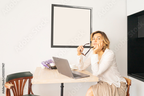 Cute young teenager girl in glasses leads video calls on a laptop. Happy pretty woman student looking at computer screen, watching webinar or doing video chat on webcam photo