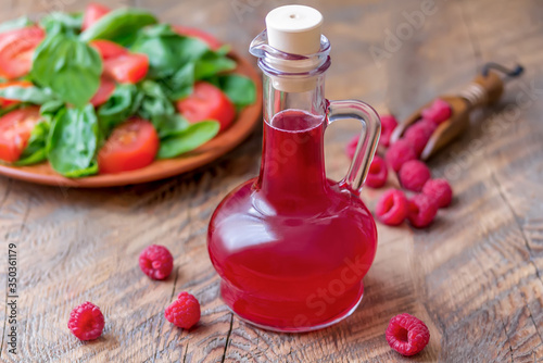 Slika na platnu Raspberry vinegar/vinaigrette salad dressing in glass cruet on a wooden background with plate of salad and fresh berries