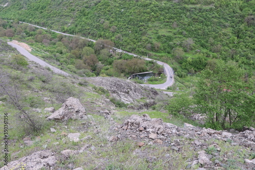 Below the rock is a road. In front of a hill with forests. A highway is located on the banks of the river. There is a car on the bridge. The air is clean and fresh