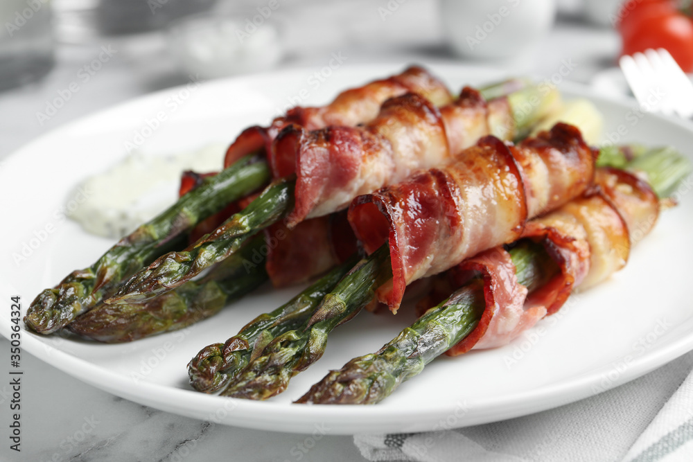 Oven baked asparagus wrapped with bacon on plate, closeup