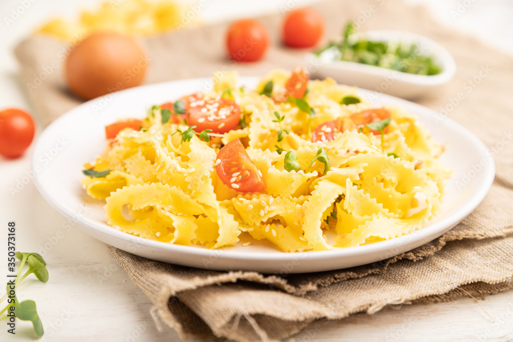 Reginelle semolina pasta with tomato, eggs, sesame and microgreen sprouts on a white wooden background. Side view, selective focus. Reginelle semolina pasta with tomato, eggs, sesame and microgreen sprouts on a white wooden background. Side view, selective focus.