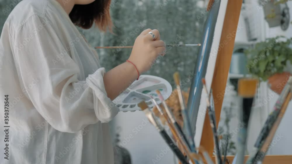 plano lateral de niña joven con bata blanca pintando obra de arte en exterior