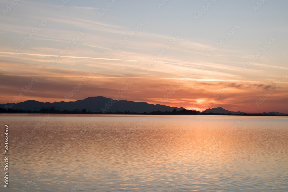 sunset over the sea and mountain in distance | landscape photography with vibrant colors in horizontal orientation | calm water and burning sky | sky behind the hills