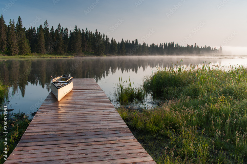 Canoe on a dock at a lake during a misty sunrise.